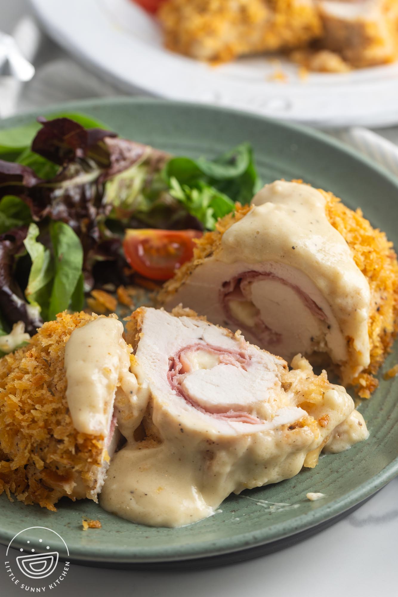 a green plate holding chicken cordon bleu and salad. The chicken has been sliced to show the han and cheese inside.