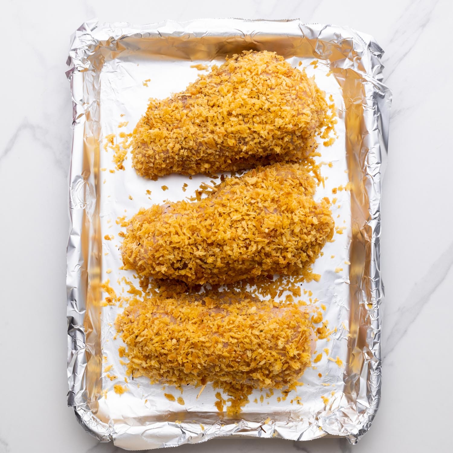 breaded chicken cordon bleu stuffed chicken breasts on a foil lined baking sheet.