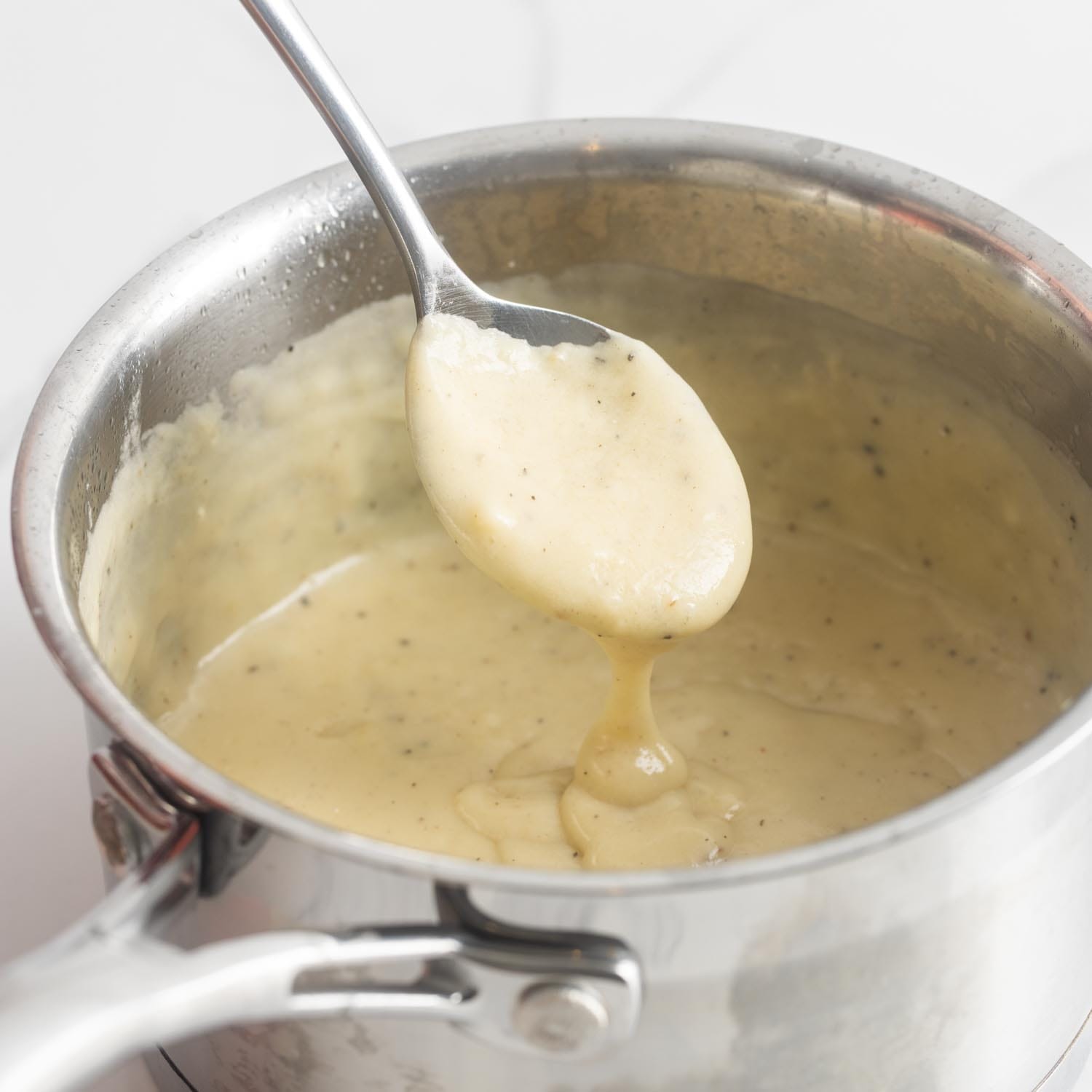 homemade creamy dijon sauce for chicken cordon bleu in a small metal saucepan with a teaspoon.