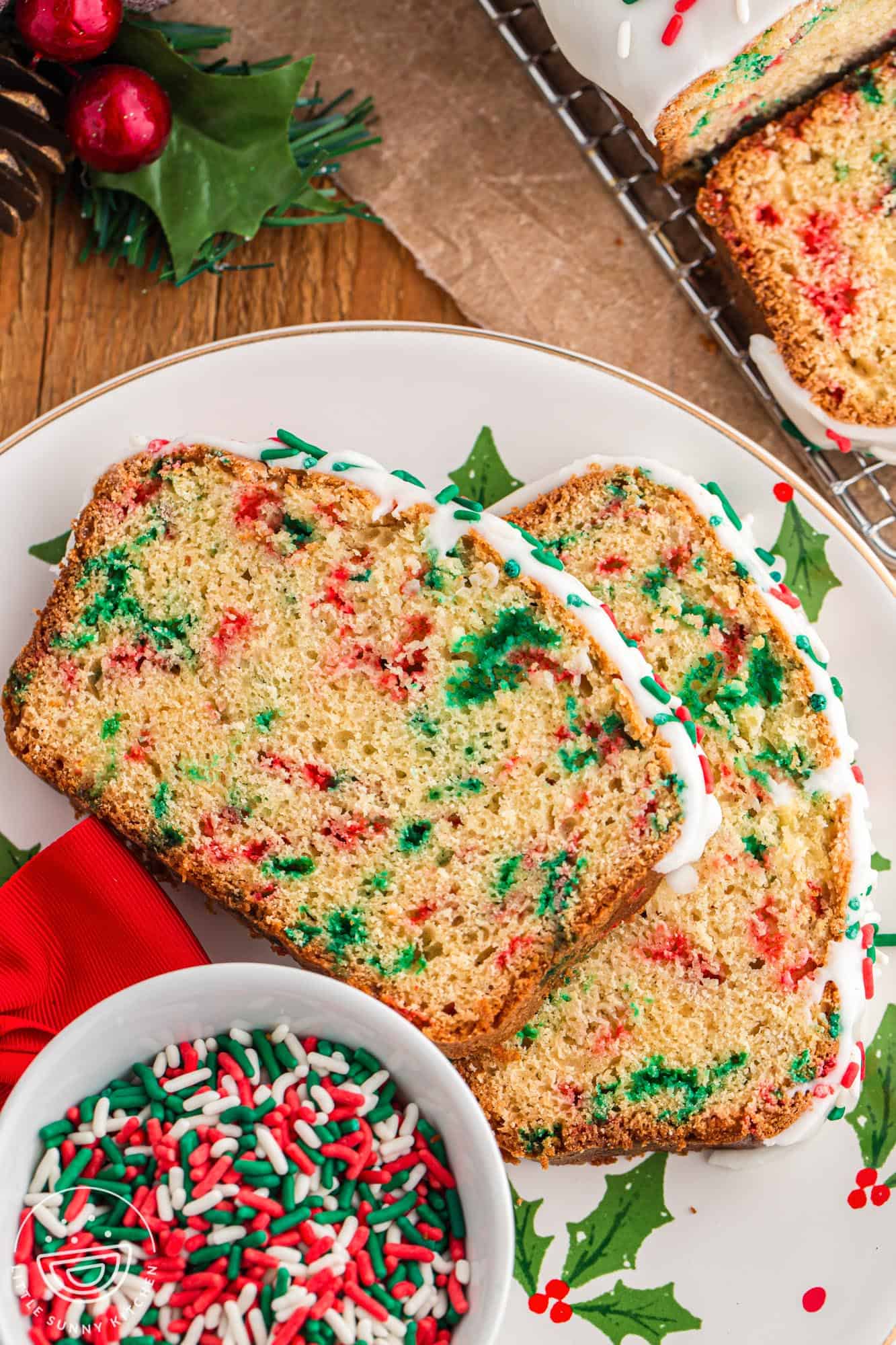 two slices of christmas bread on a christmas plate along with a small ramekin of christmas sprinkles.