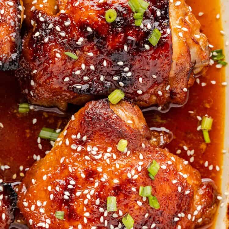 two bone in chicken thighs with honey soy sauce in a baking dish, garnished with sesame seeds.