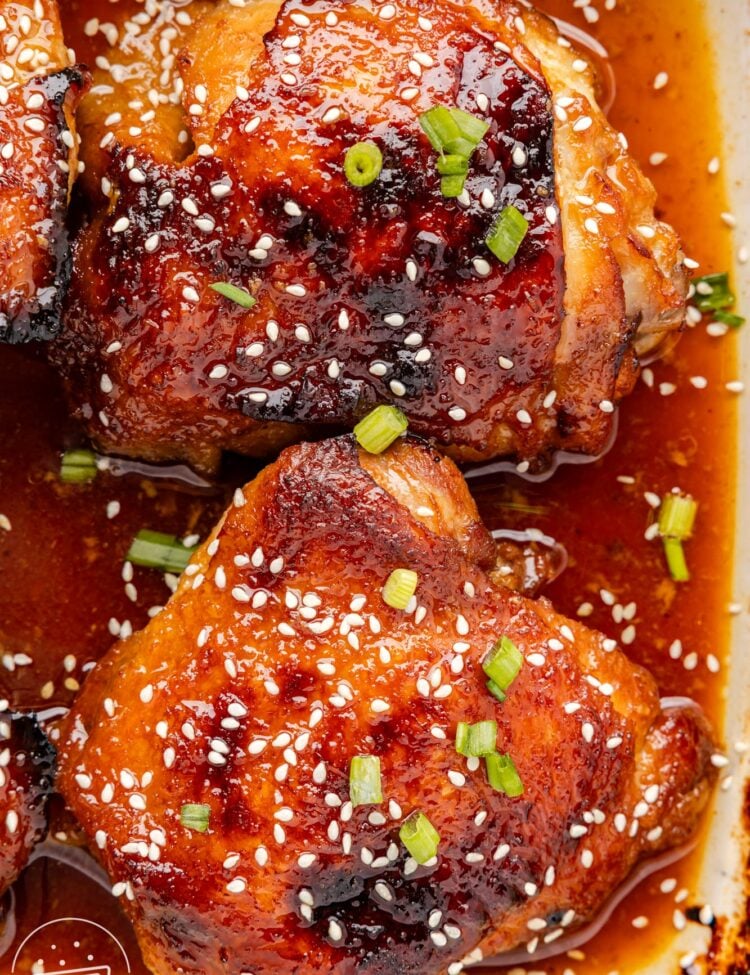 two bone in chicken thighs with honey soy sauce in a baking dish, garnished with sesame seeds.