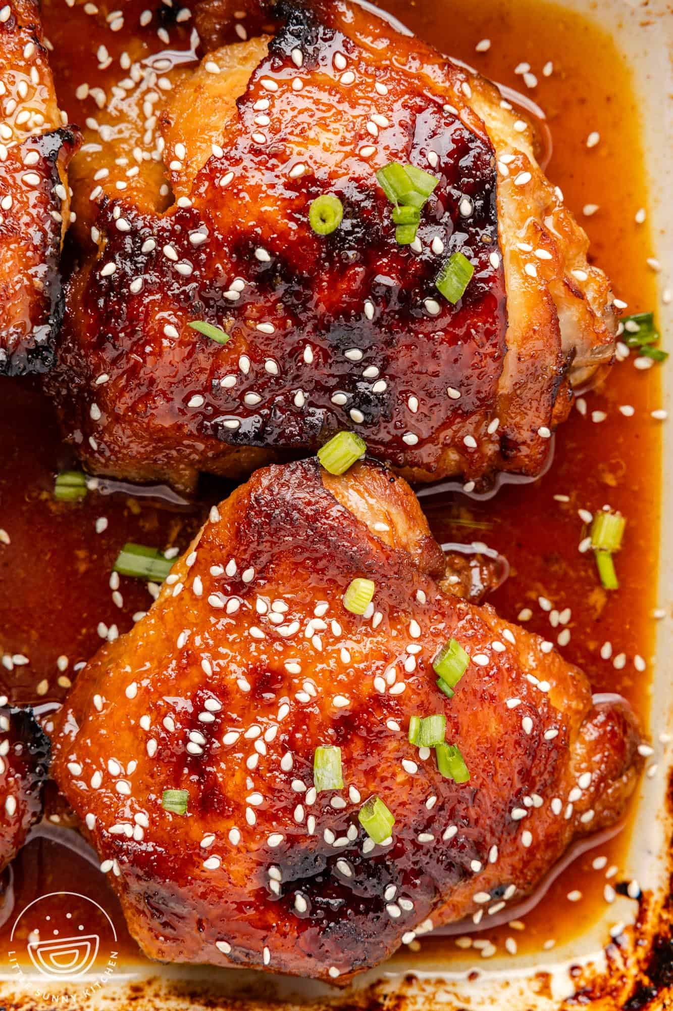 two bone in chicken thighs with honey soy sauce in a baking dish, garnished with sesame seeds.