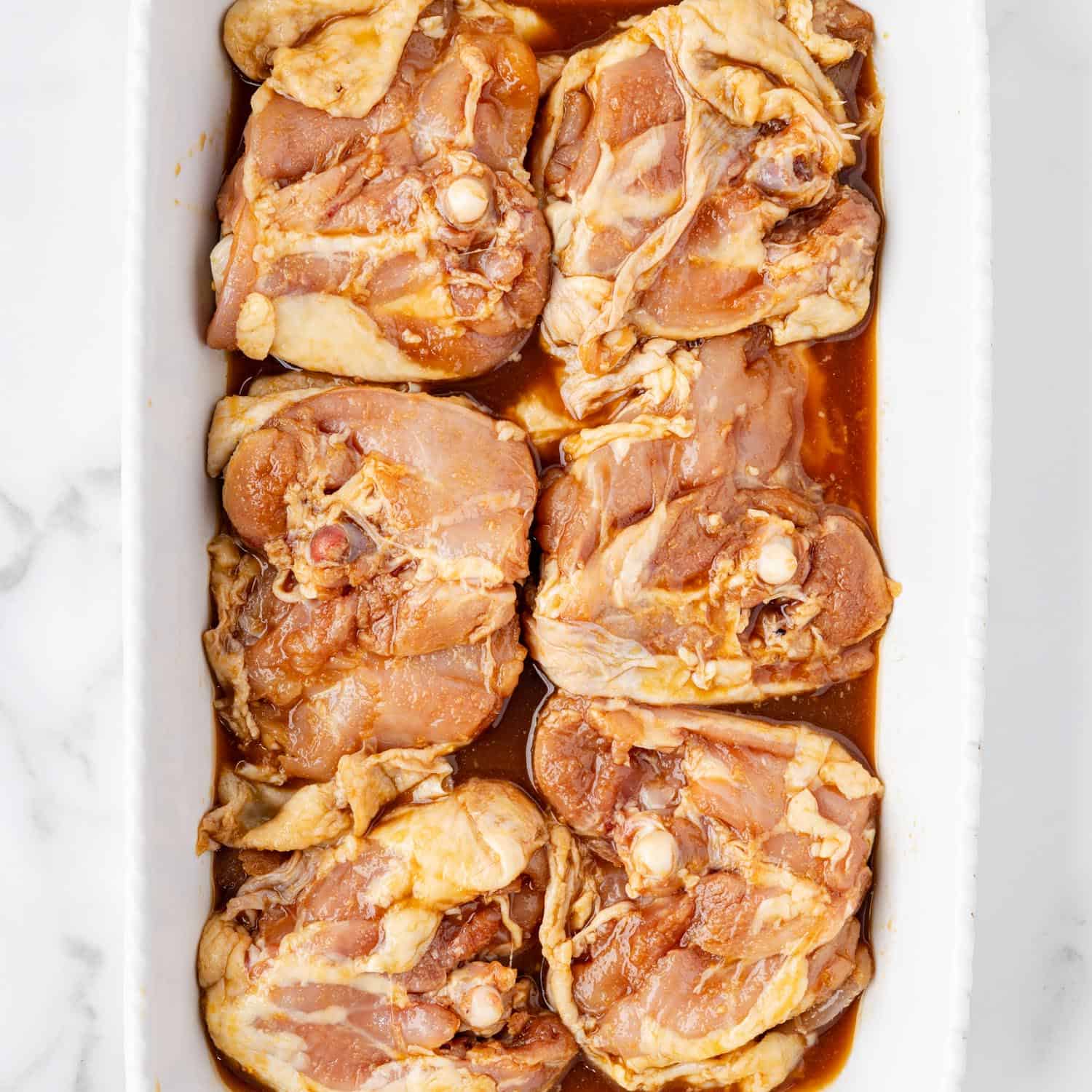 honey soy marinated chicken thighs, skin side down, in a white ceramic baking pan.