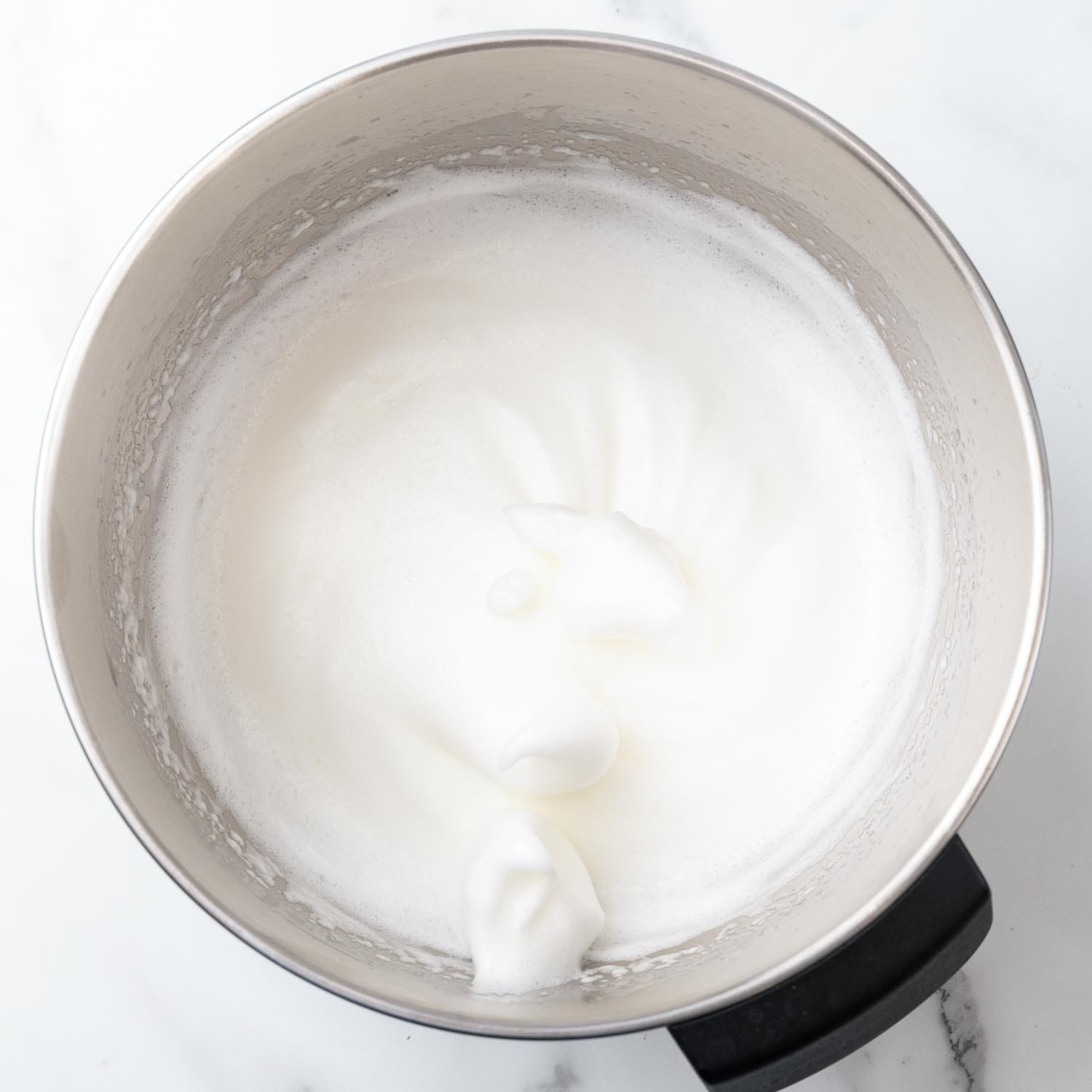 egg whites whipped to stiff peaks in a metal mixing bowl.