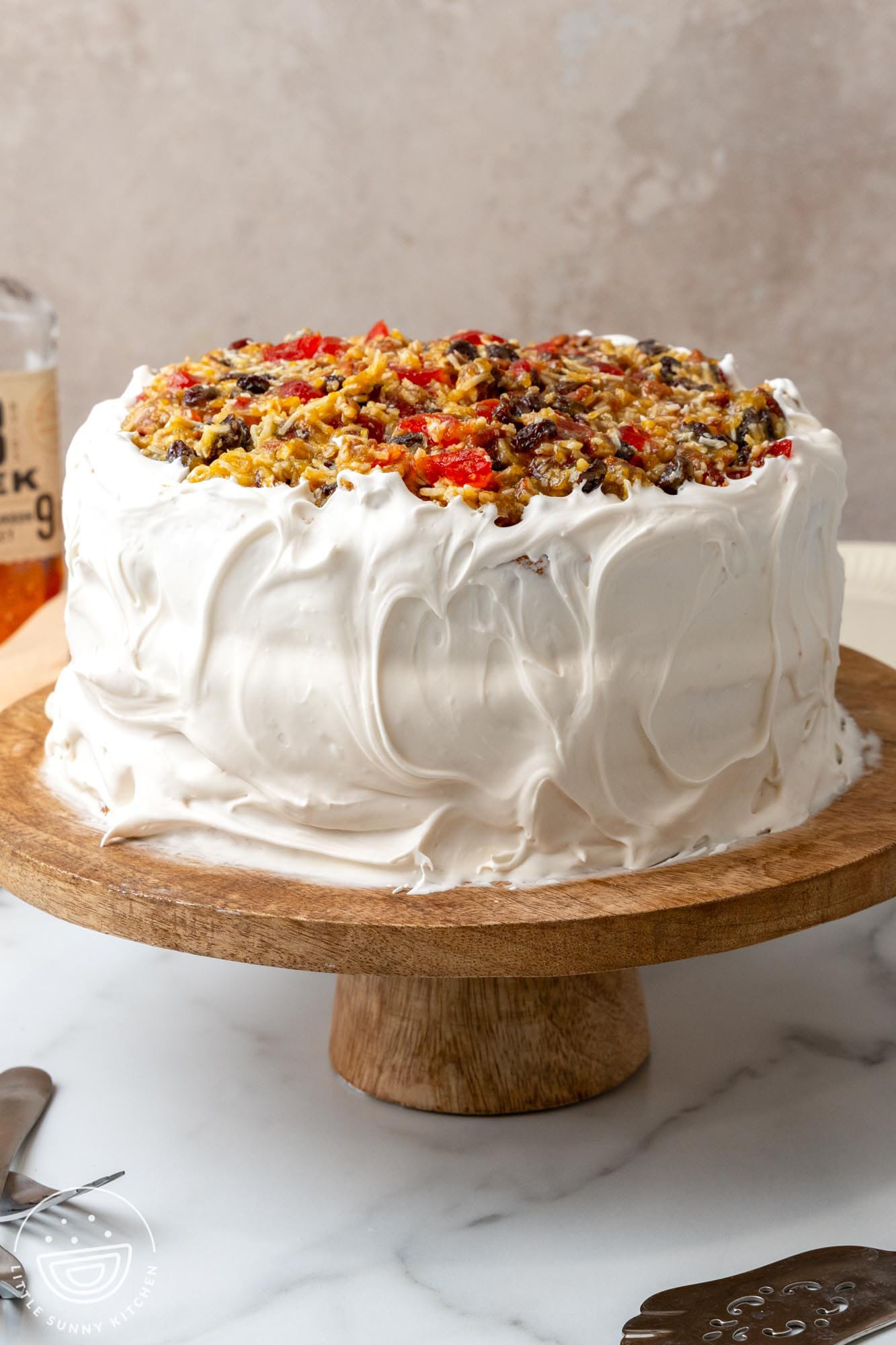 A whole lane cake covered in 7 minute frosting and topped with a mixture of nuts, coconut, cherries and raisins.