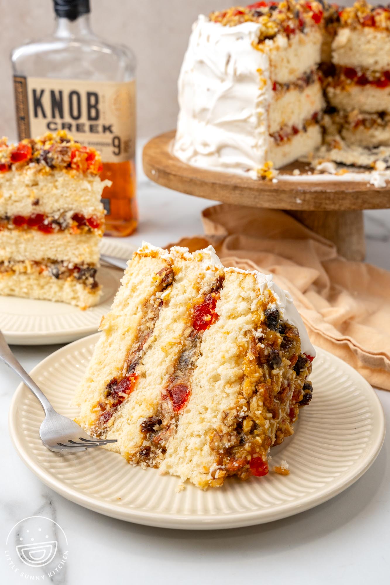 slices of lane cake on plates in front of a whole cake and a bottle of whisky.