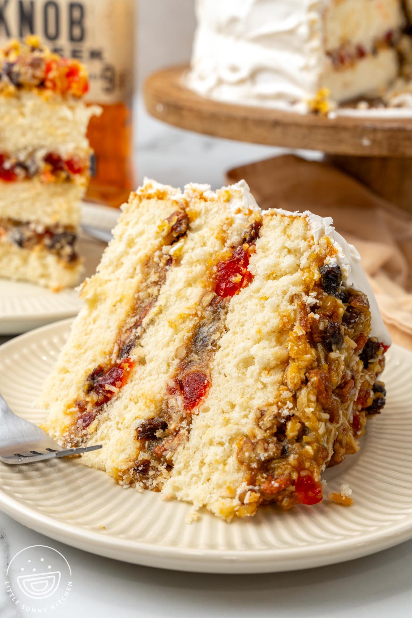 a large slice of lane layer cake with candied cherries and nuts, on a plate.