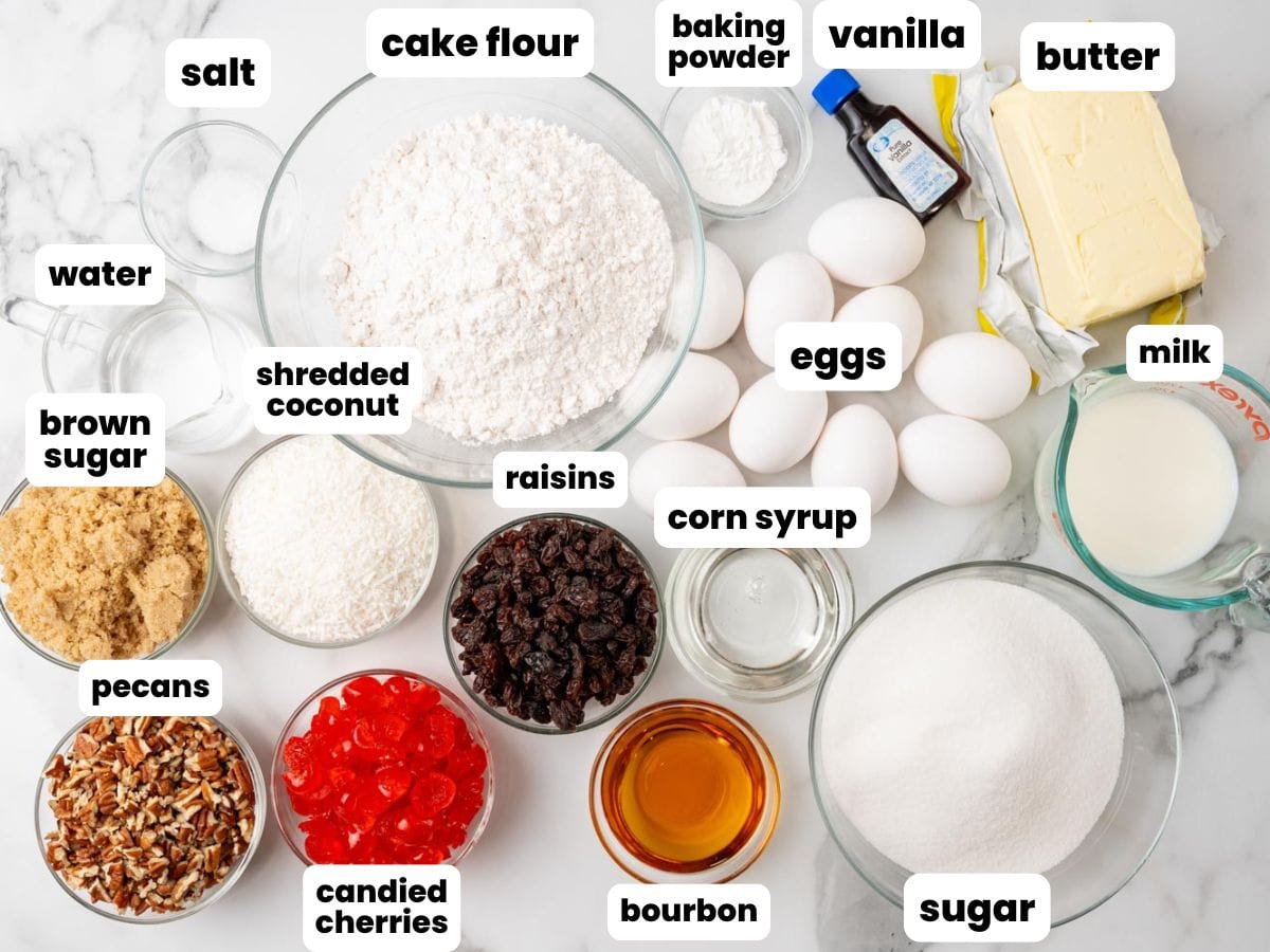 Lane cake ingredients including cherries, raisins, coconut, and 10 eggs, all in small bowls on a marble counter.