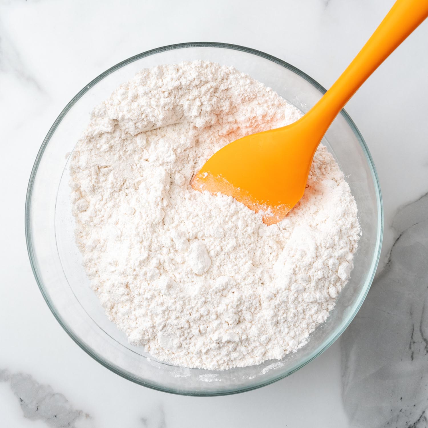 cake flour, baking powder, and salt mixed in glass bowl with an orange spatula.