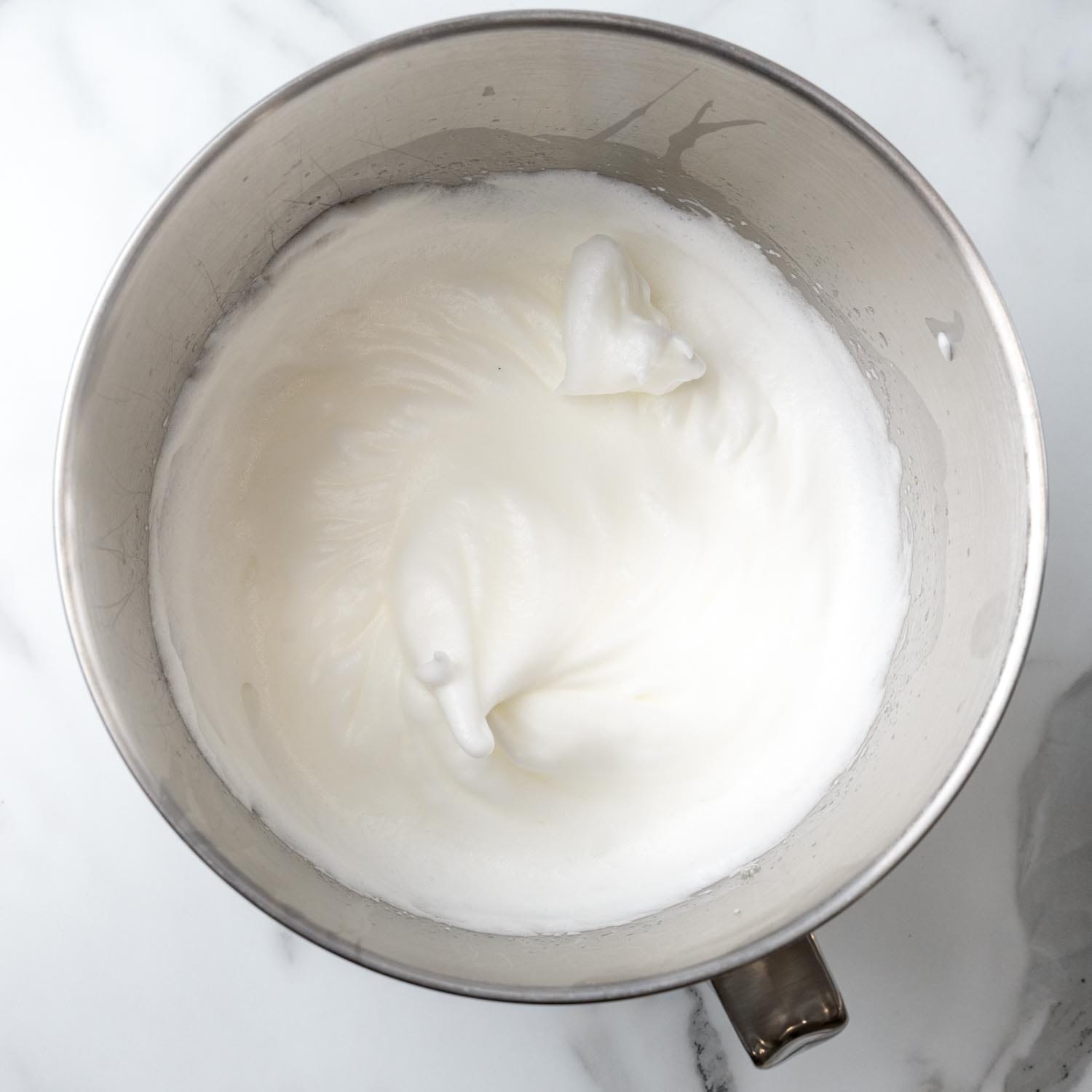 egg whites whipped to stiff peaks in a metal mixing bowl.