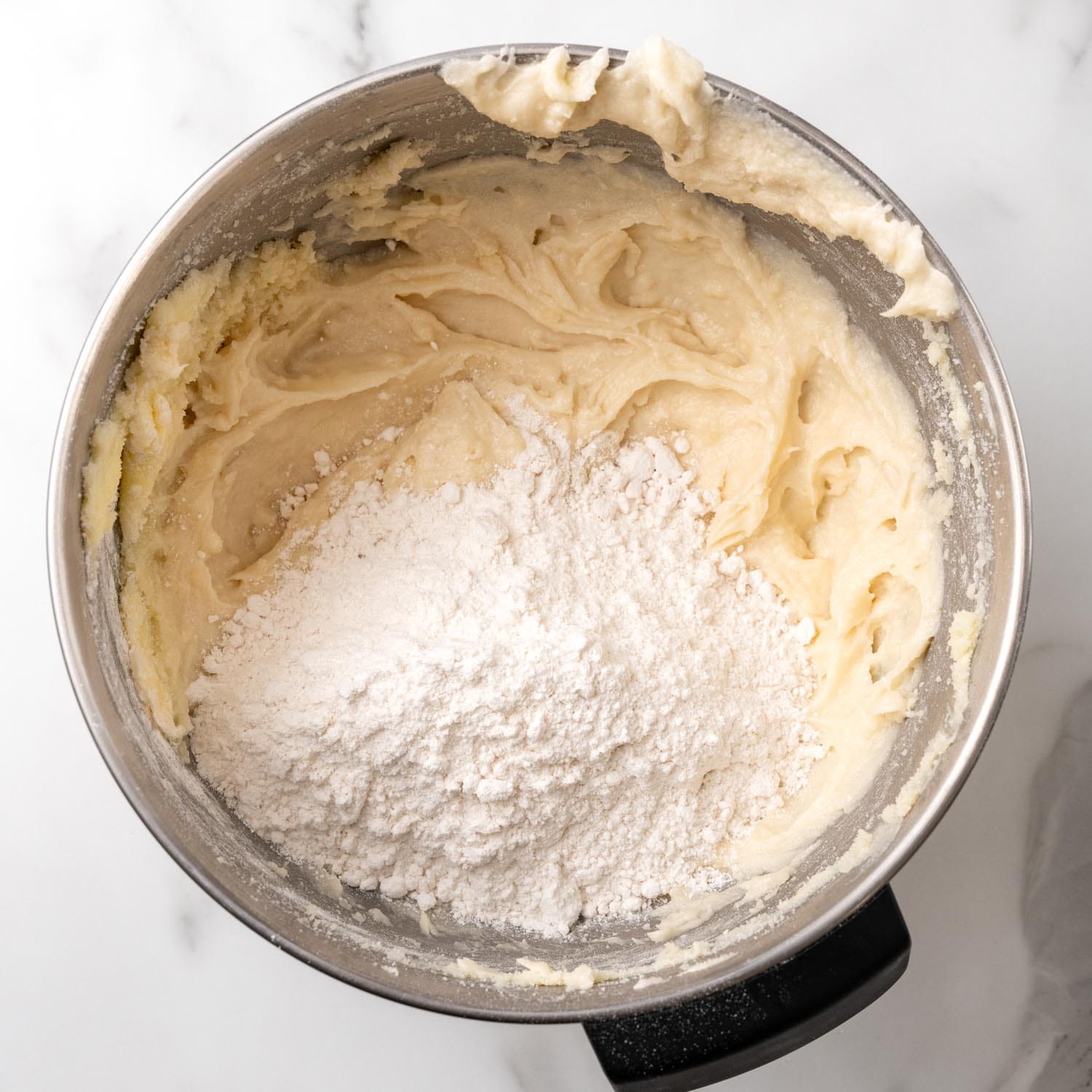 flour added to cake batter in a metal mixing bowl.