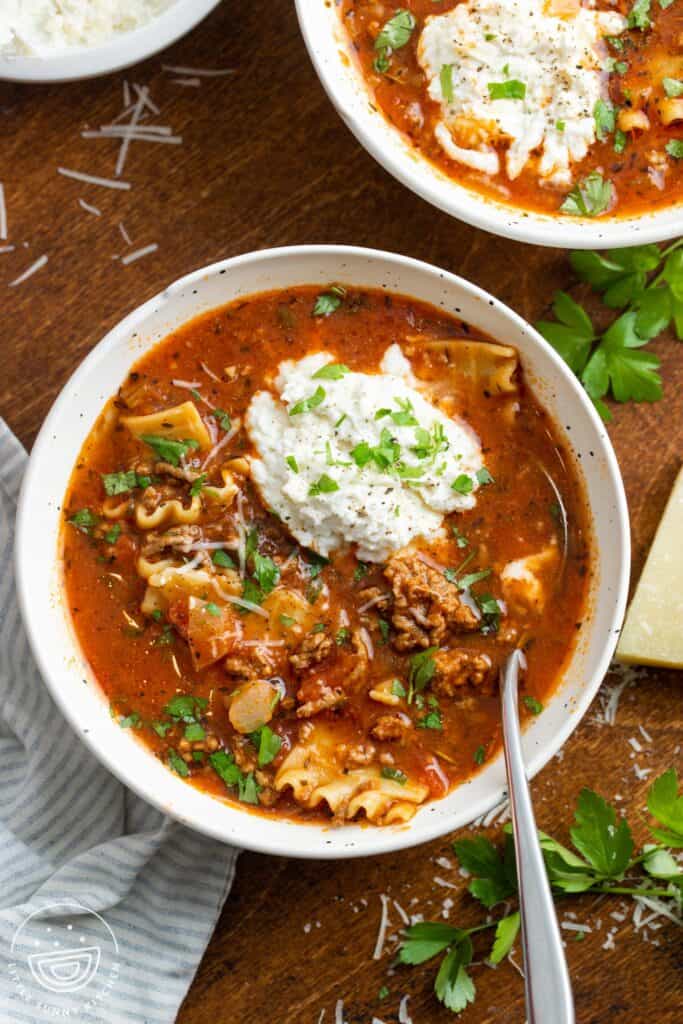 overhead view of a bowl of lasagna soup with a scoop of ricotta cheese and a garnish of fresh basil leaves.