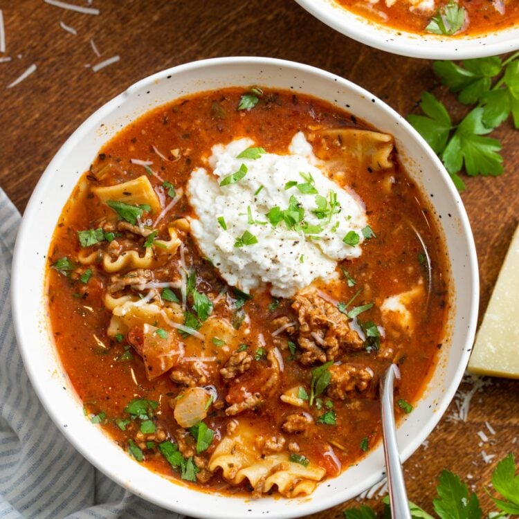 overhead view of a bowl of lasagna soup with a scoop of ricotta cheese and a garnish of fresh basil leaves.