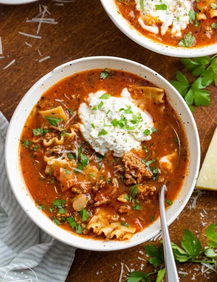overhead view of a bowl of lasagna soup with a scoop of ricotta cheese and a garnish of fresh basil leaves.
