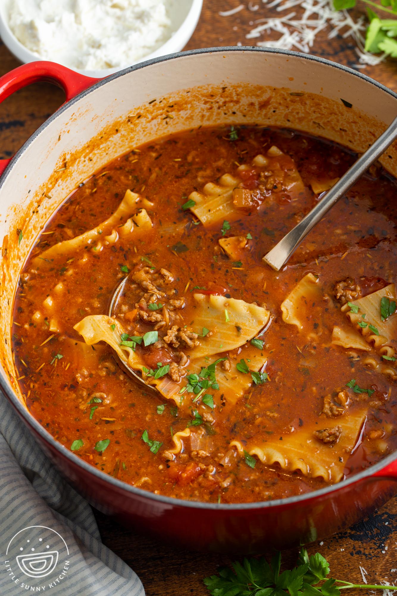 A red dutch oven with lasagna soup and a ladle