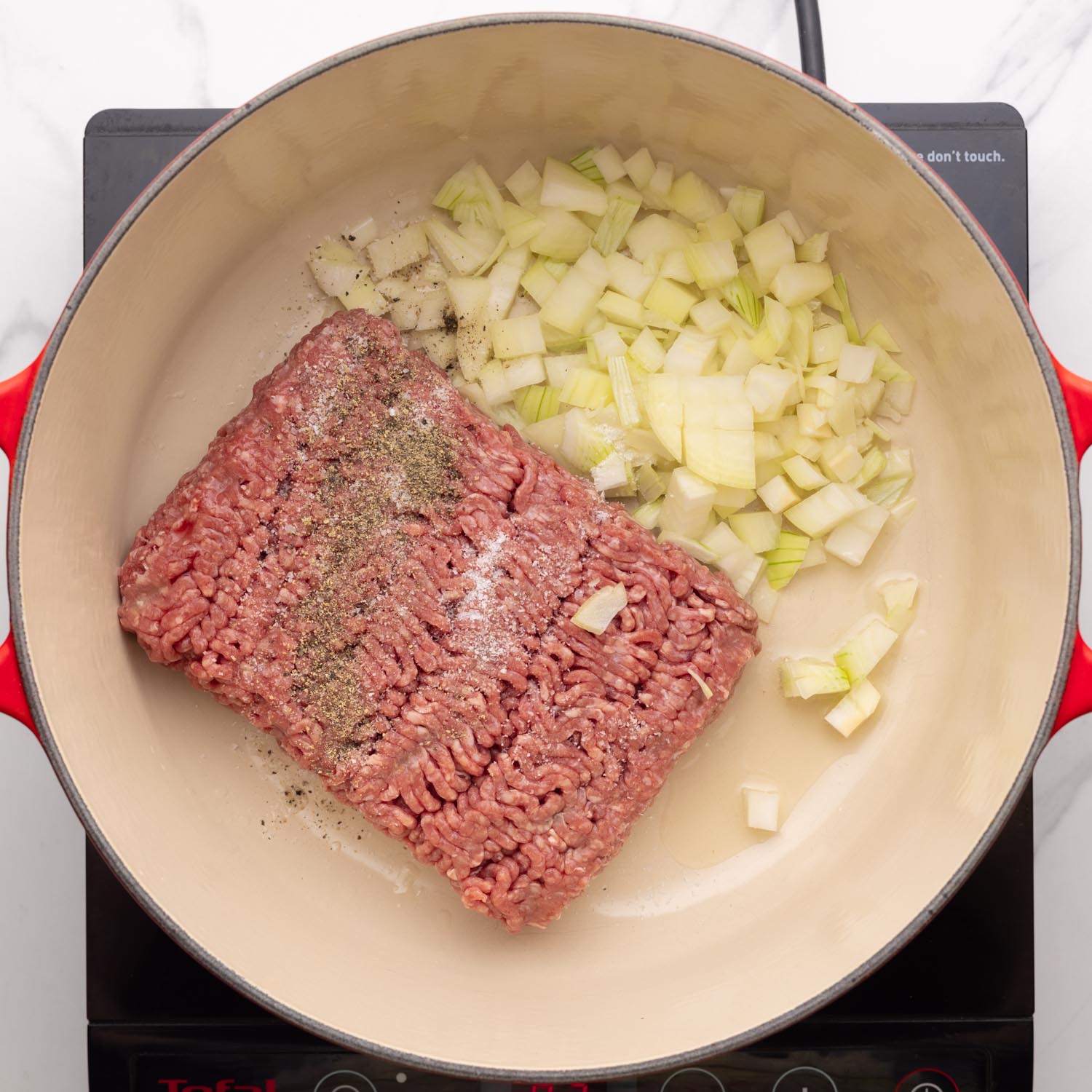 ground beef, diced onions, and seasonings added to a dutch oven with olive oil.