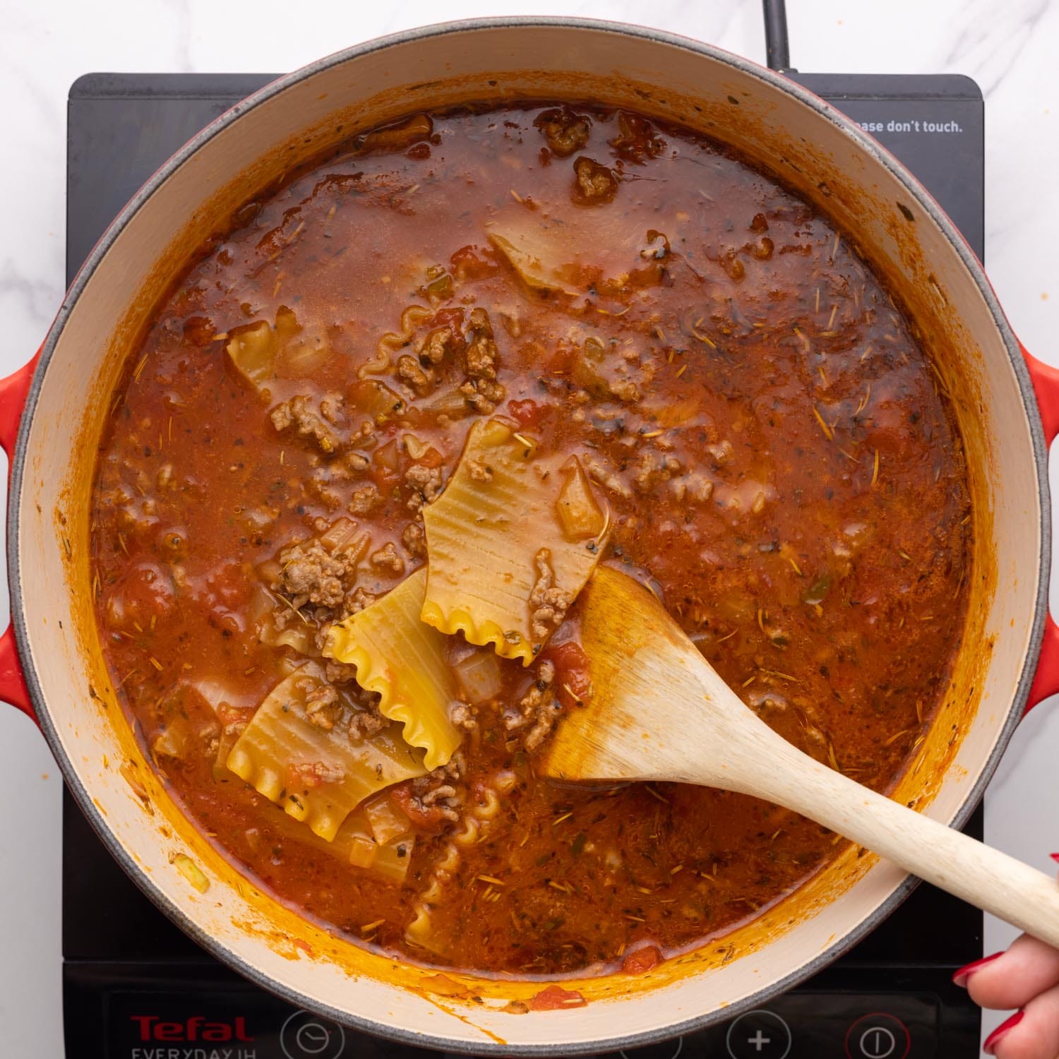 overhead view of a white dutch oven filled with lasagna soup with large pieces of lasagna noodles in a tomato based broth.