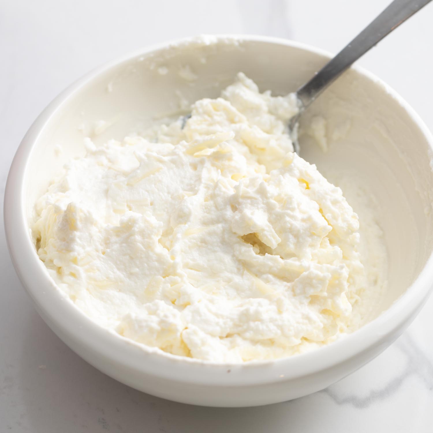 a glass bowl of ricotta cheese mixed with parmesan and mozzarella