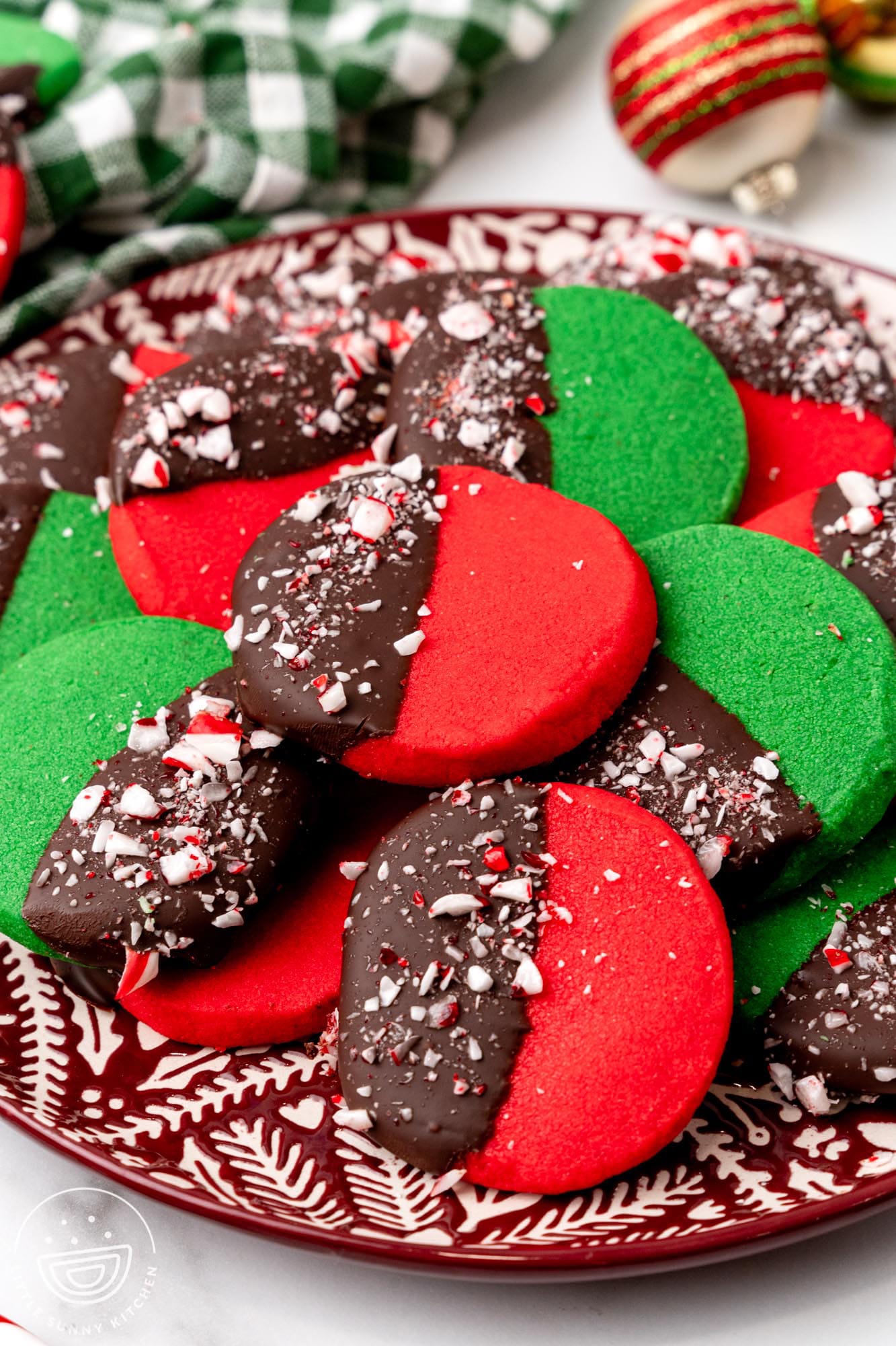 a ceramic plate holding peppermint shortbread cookies. These are round cookies, dyed red and green and dipped in chocolate and peppermint candy.