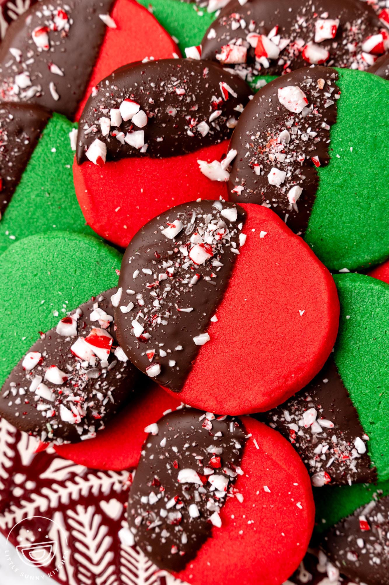 dark red and deep green round shortbread cookies. Each cookie is half dipped in chocolate and decorated with crushed peppermint candy.