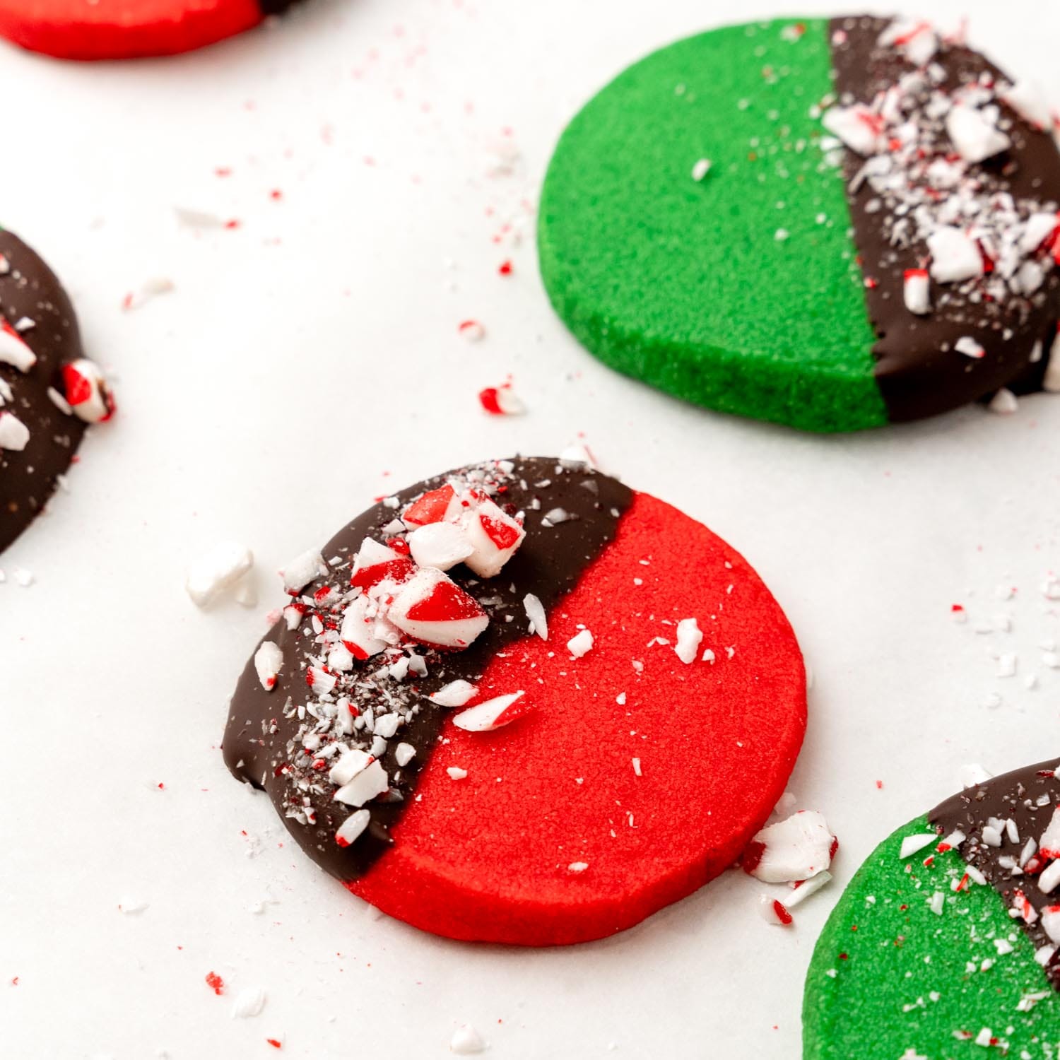 Closeup of red and green shortbread cookies that have been dipped in chocolate with crushed candy cane pieces on top.