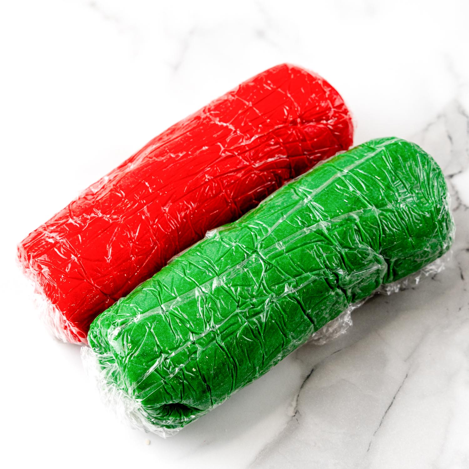 logs of red and green cookie dough, wrapped in plastic wrap.