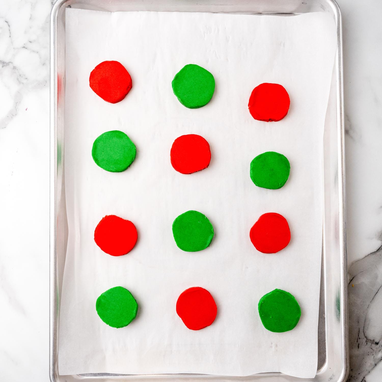 unbaked round red and green shortbread cookies on a parchment lined baking sheet.