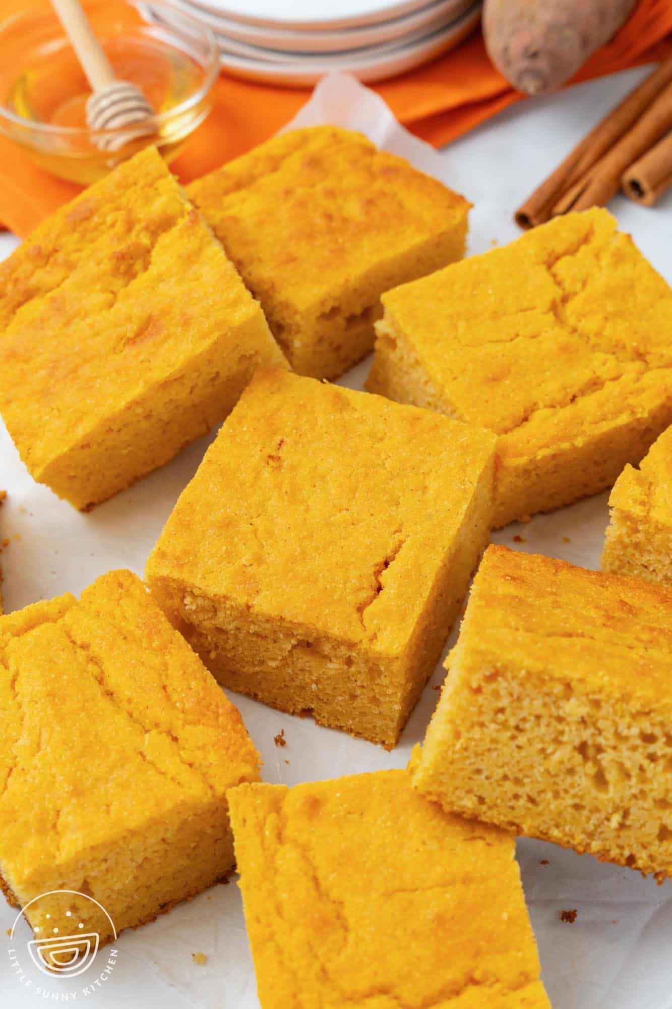 squares of sweet potato cornbread on a counter. In the background are honey and cinnamon sticks.