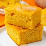 two square pieces of sweet potato cornbread on a plate. Honey is drizzled over.