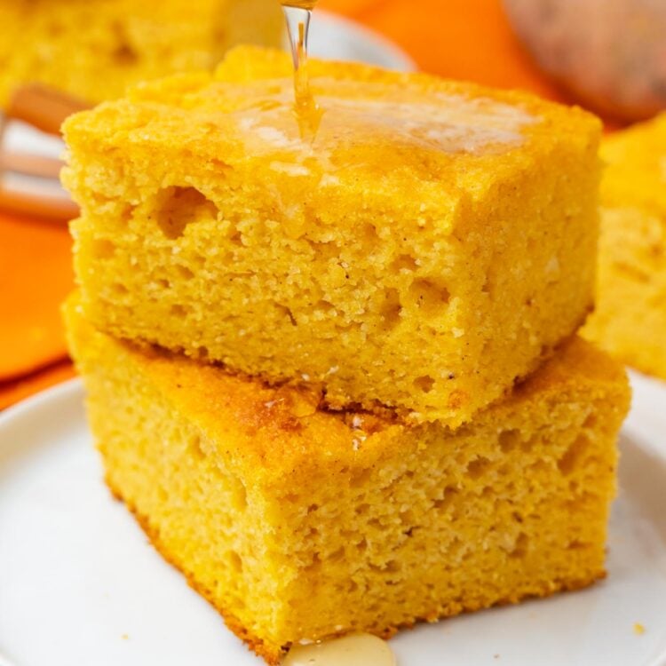 two square pieces of sweet potato cornbread on a plate. Honey is drizzled over.