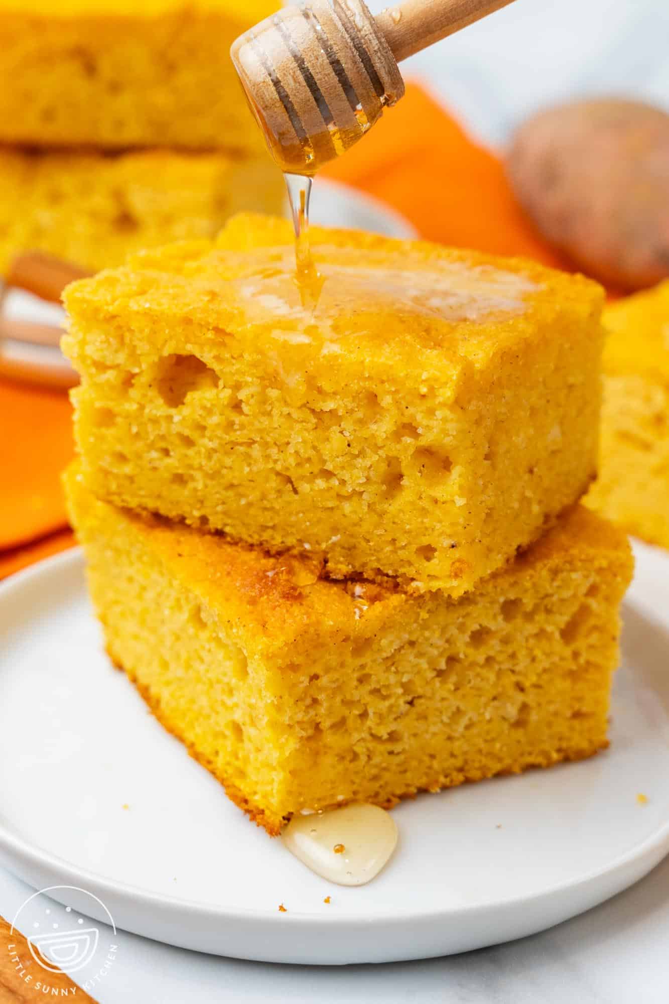 two square pieces of sweet potato cornbread on a plate. Honey is drizzled over.