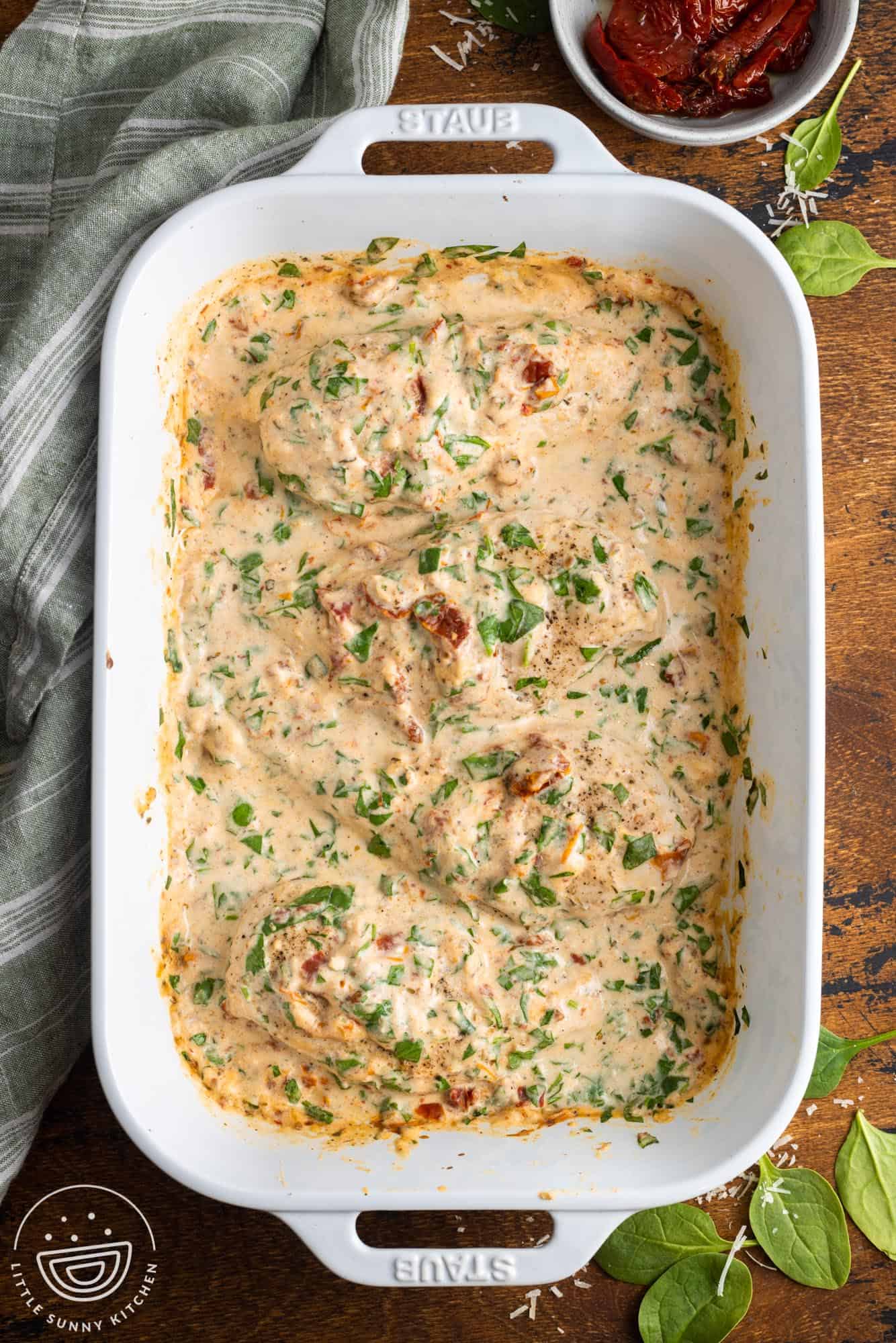 Baked tuscan chicken breasts in a creamy spinach and sundried tomato sauce in a white casserole pan.