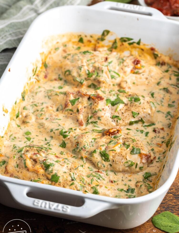 a white casserole dish of baked chicken in a creamy spinach tuscan sauce.