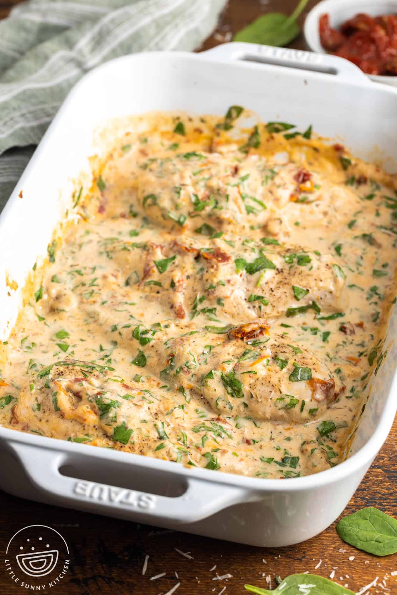 a white casserole dish of baked chicken in a creamy spinach tuscan sauce.