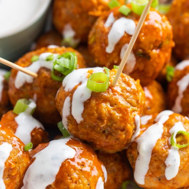 closeup of buffalo chicken meatballs, drizzled with blue cheese, with toothpicks for serving.