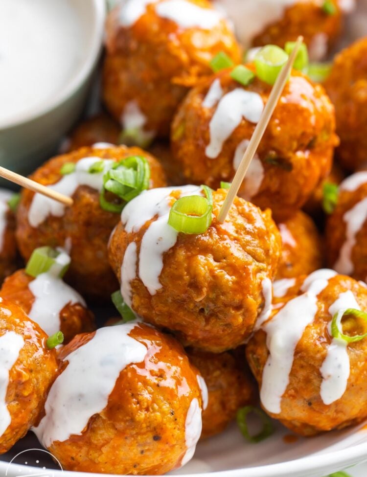 closeup of buffalo chicken meatballs, drizzled with blue cheese, with toothpicks for serving.