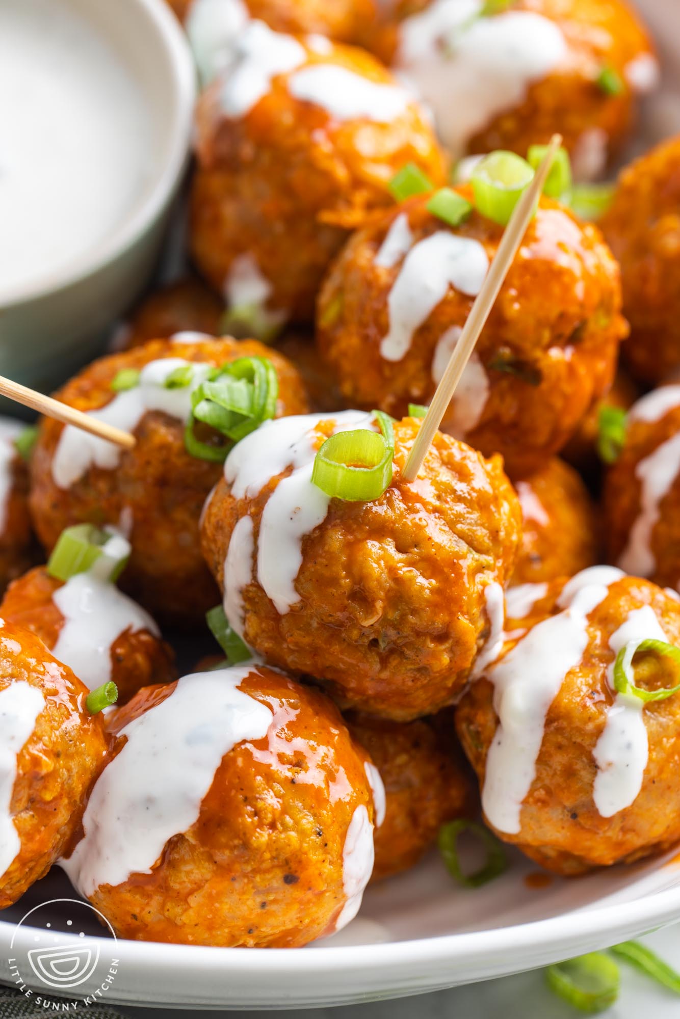 closeup of buffalo chicken meatballs, drizzled with blue cheese, with toothpicks for serving.