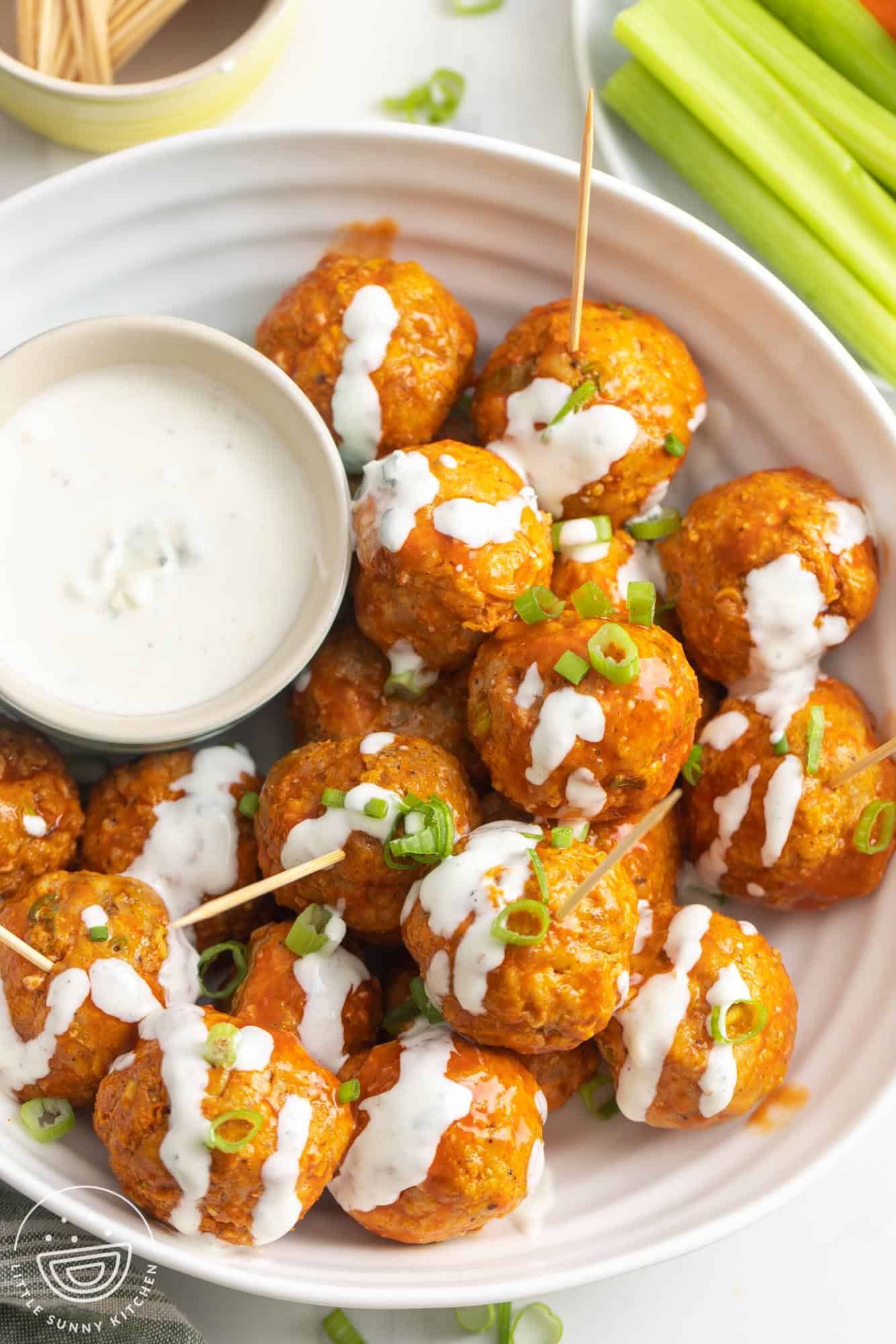 a plate of buffalo chicken meatballs with blue cheese dressing. Toothpicks are inserted into some of the meatballs.