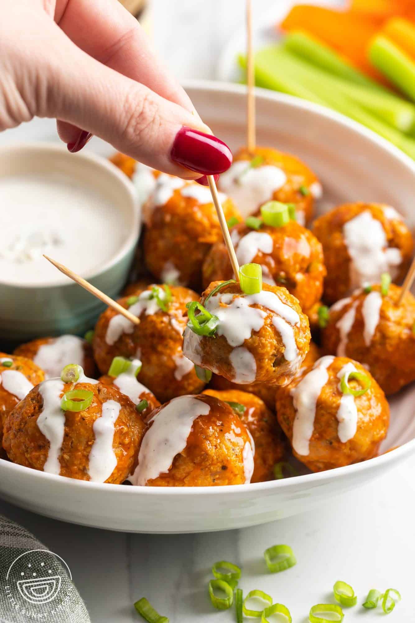 a hand picking up a buffalo style chicken meatball with a toothpick.