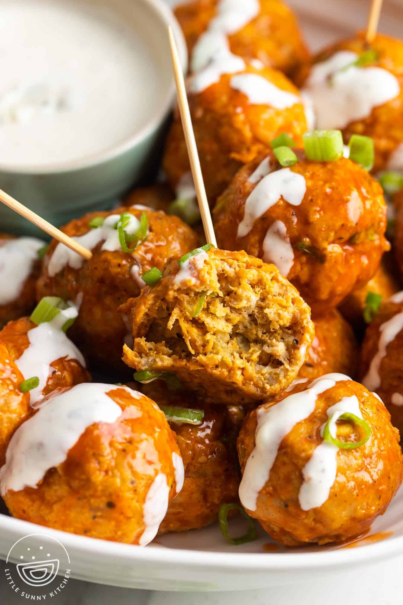 a plate of buffalo chicken meatballs. One has a bite taken to show the tender inside texture.