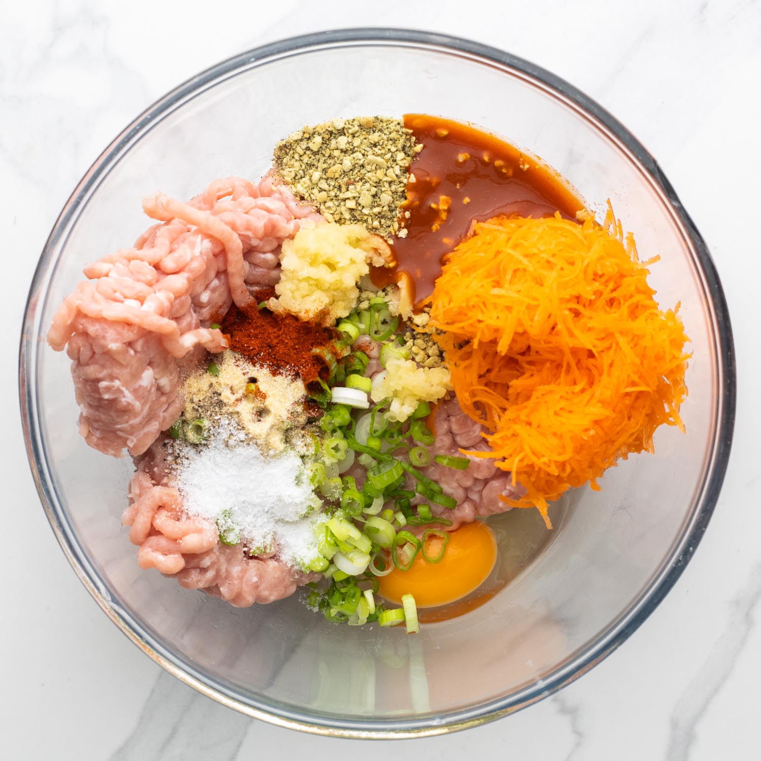 Ground chicken in a glass bowl with buffalo meatball ingredients including carrots, breadcrumbs, and hot sauce.