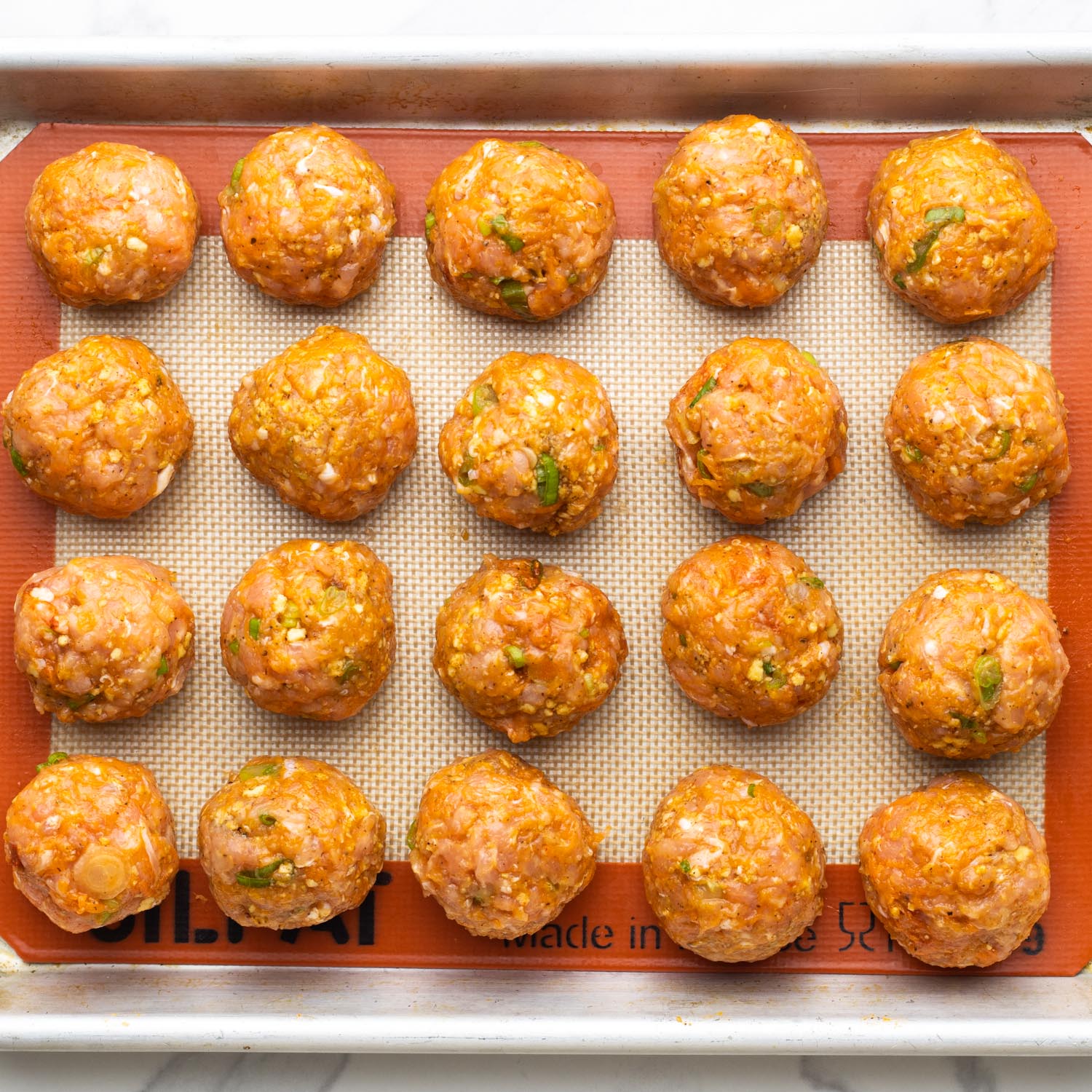 Raw buffalo chicken meatballs on a silpat lined baking tray.