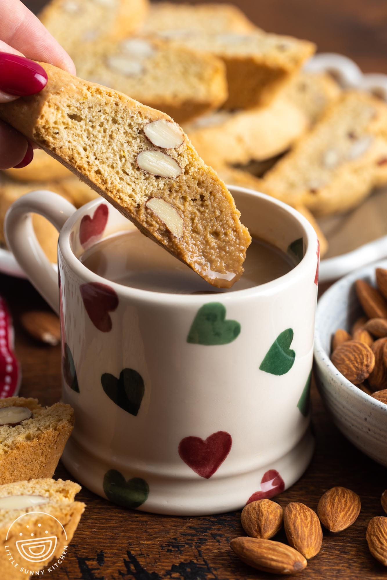 a hand dipping a cantucci into a cup of coffee. The coffee mug has small hearts on it.