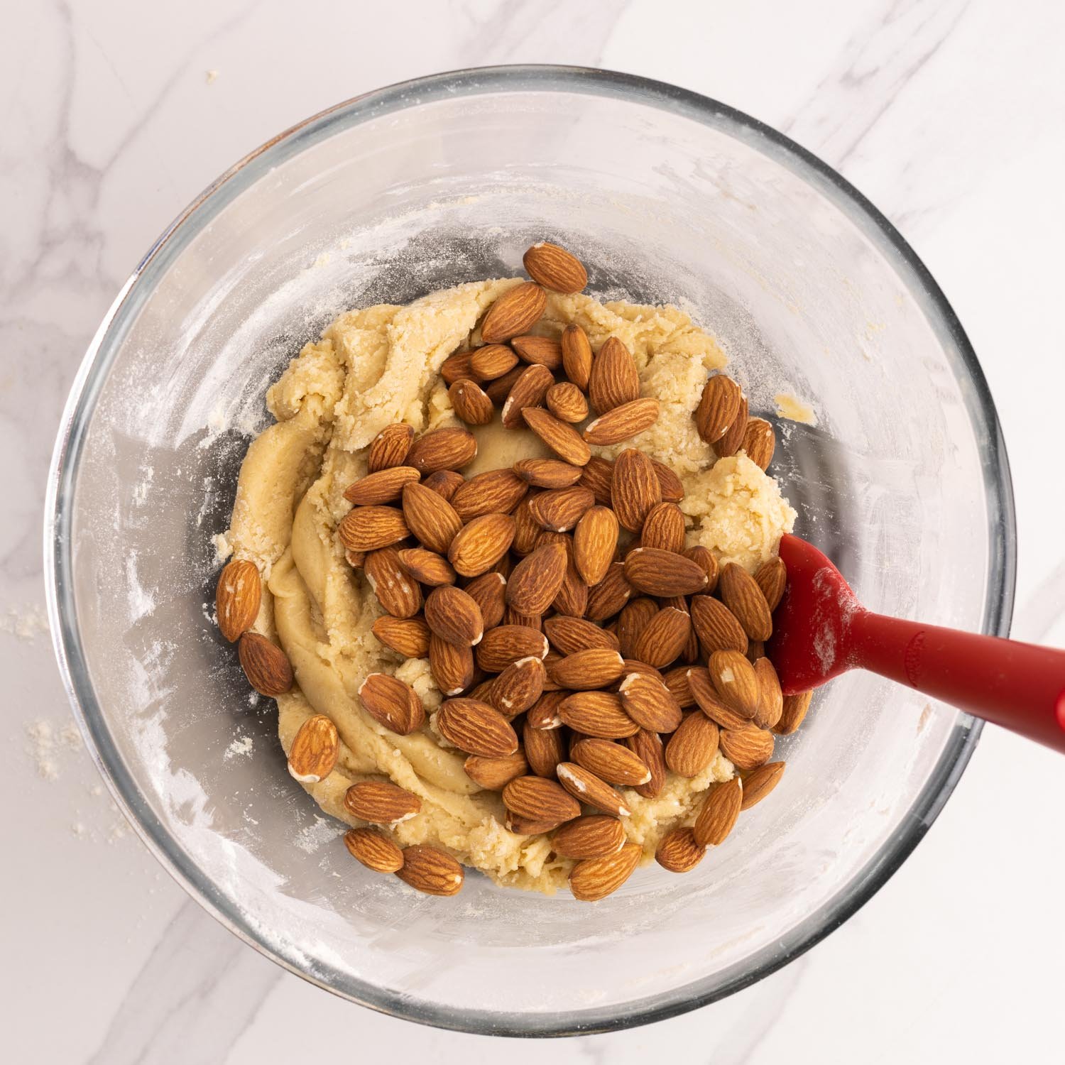 whole almonds mixed into biscotti dough in a glass bowl.