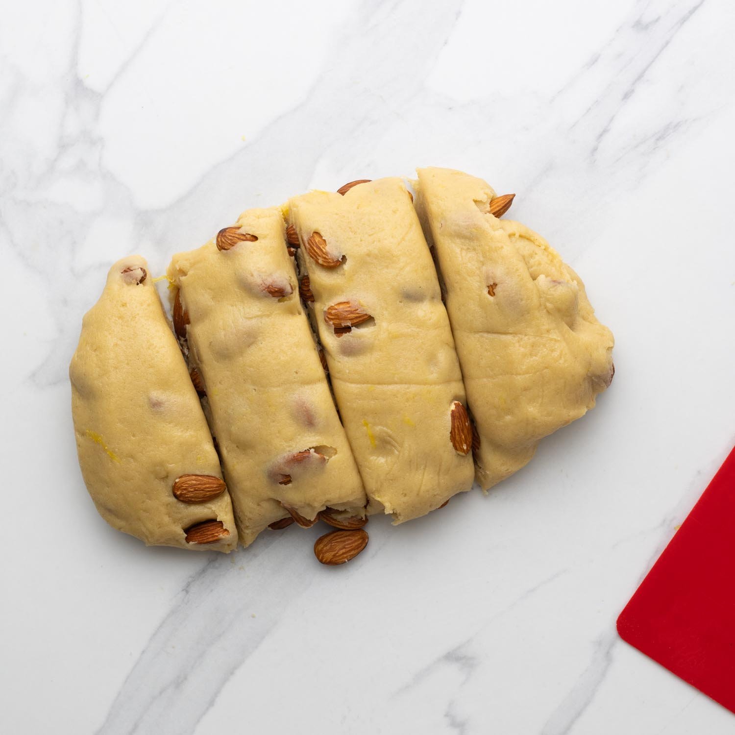 a loaf of cantucci dough, cut into four pieces on a marble counter.