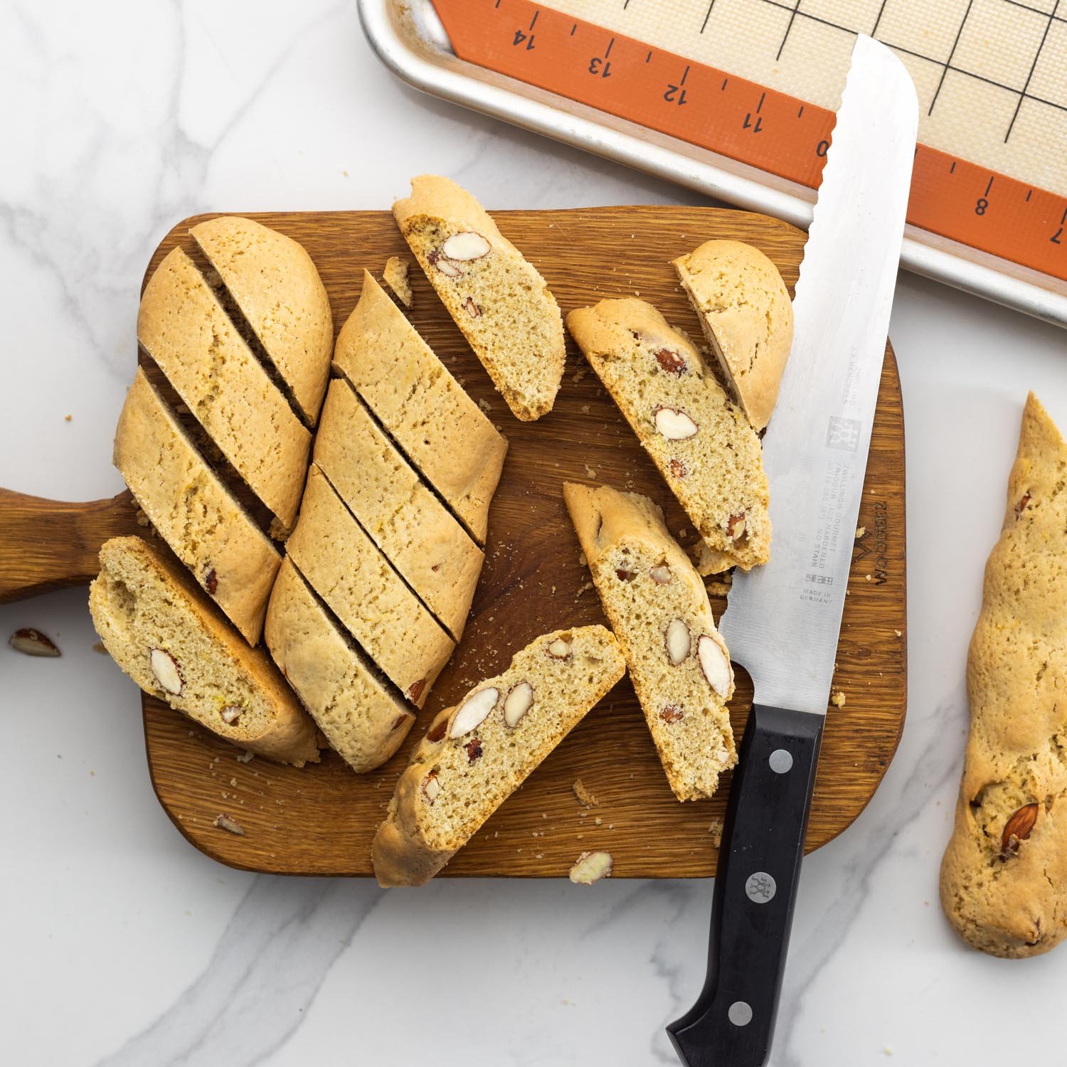 cantucci sliced into pieces with a serrated knife on a small wooden cutting board.