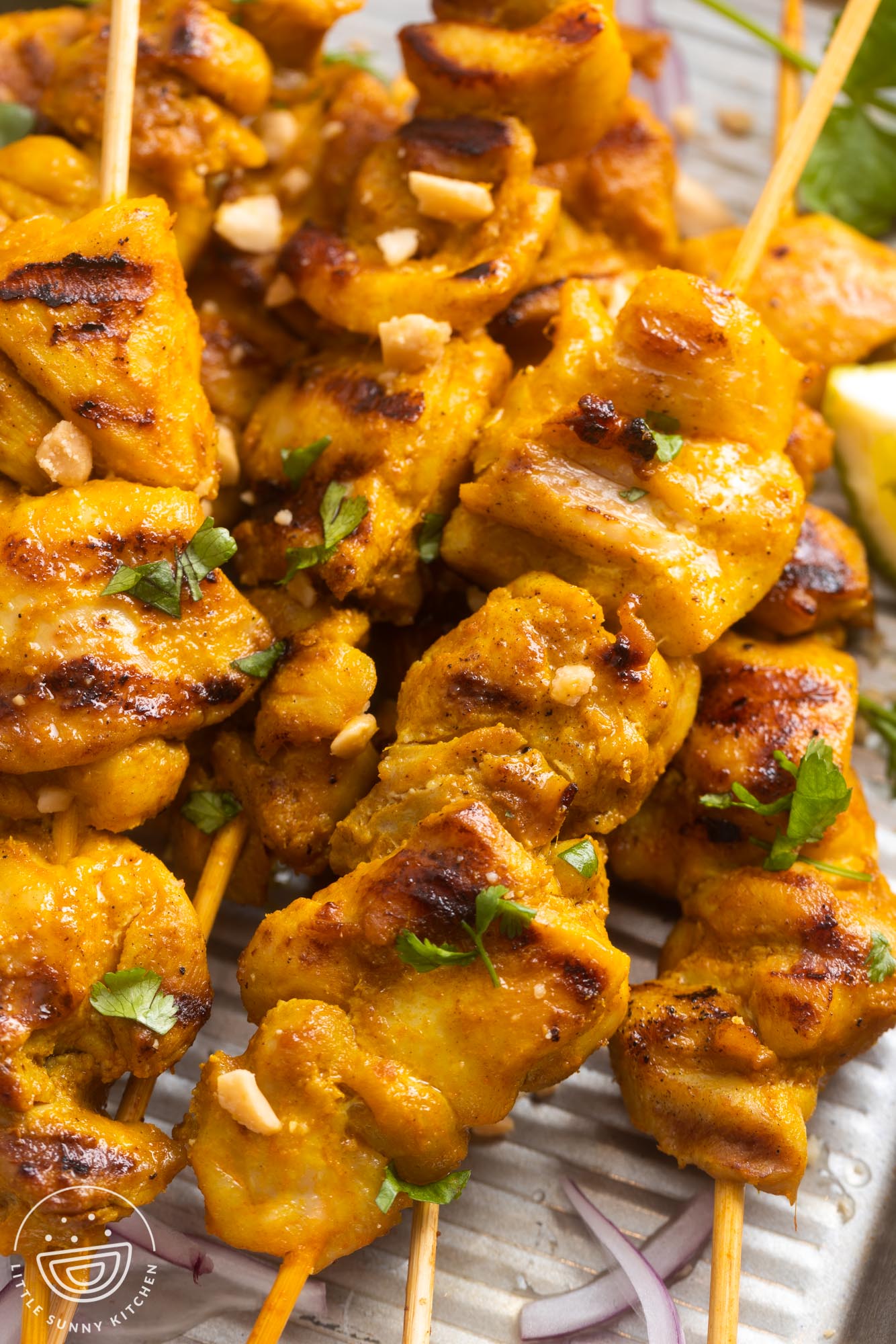 closeup of grilled chicken satay skewers topped with peanuts and cilantro.