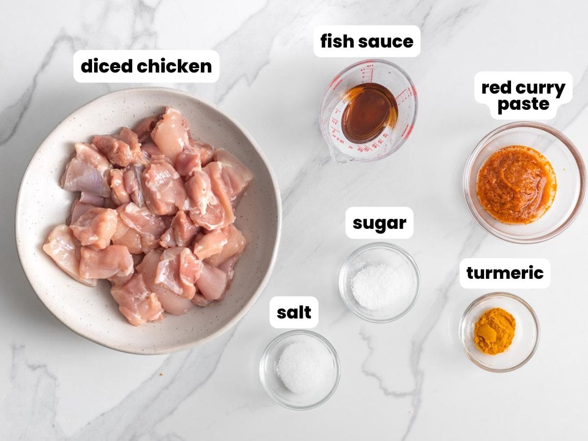 a bowl of diced chicken thighs with ingredients to make chicken satay marinade