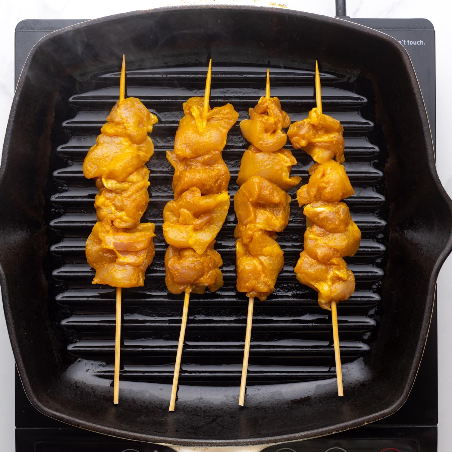 four chicken satay skewers cooking on a cast iron grill pan.